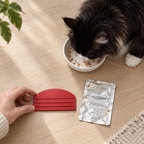 Illustrative black-and-white Maine Coon finishing its meal beside the red squeezer and flattened empty pouch