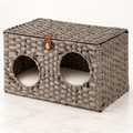 The Woven Retreat grey rattan cat house on a pale white-marble studio floor