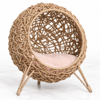 Large cat rattan pod bed with pink cushion on a light marble background