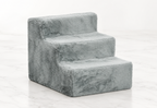 Light-grey three-step plush pet stairs on a light white marble background